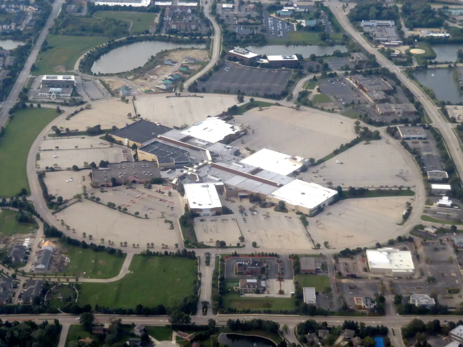 Aerial view of a large retail mall property with expansive striped parking lots, ring roads, and outparcels